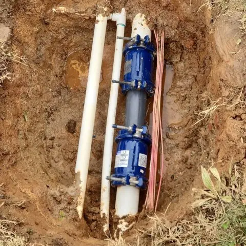 Picture of a hole in the tan to reddish rocky Georgia soil, with a water supply, also known as a water service, that has been repaired neatly oorganized next to other smaller piping