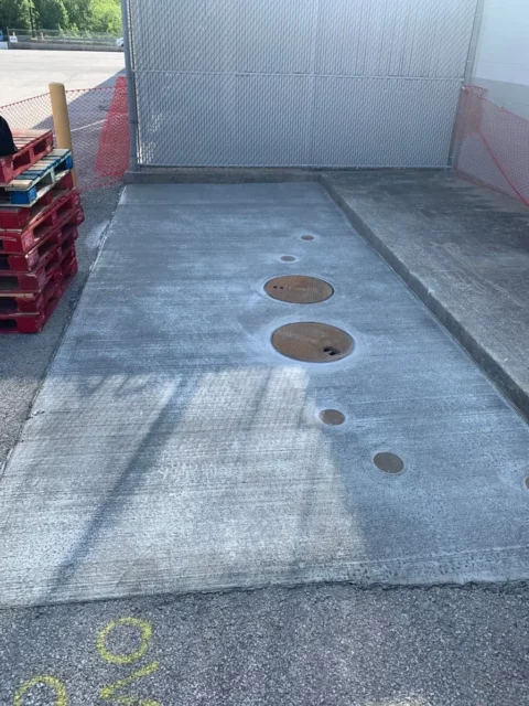 rectangle of concrete with 2 manholes and 4 additional 4 inch cleanouts showing a completed inground grease interceptor installation.