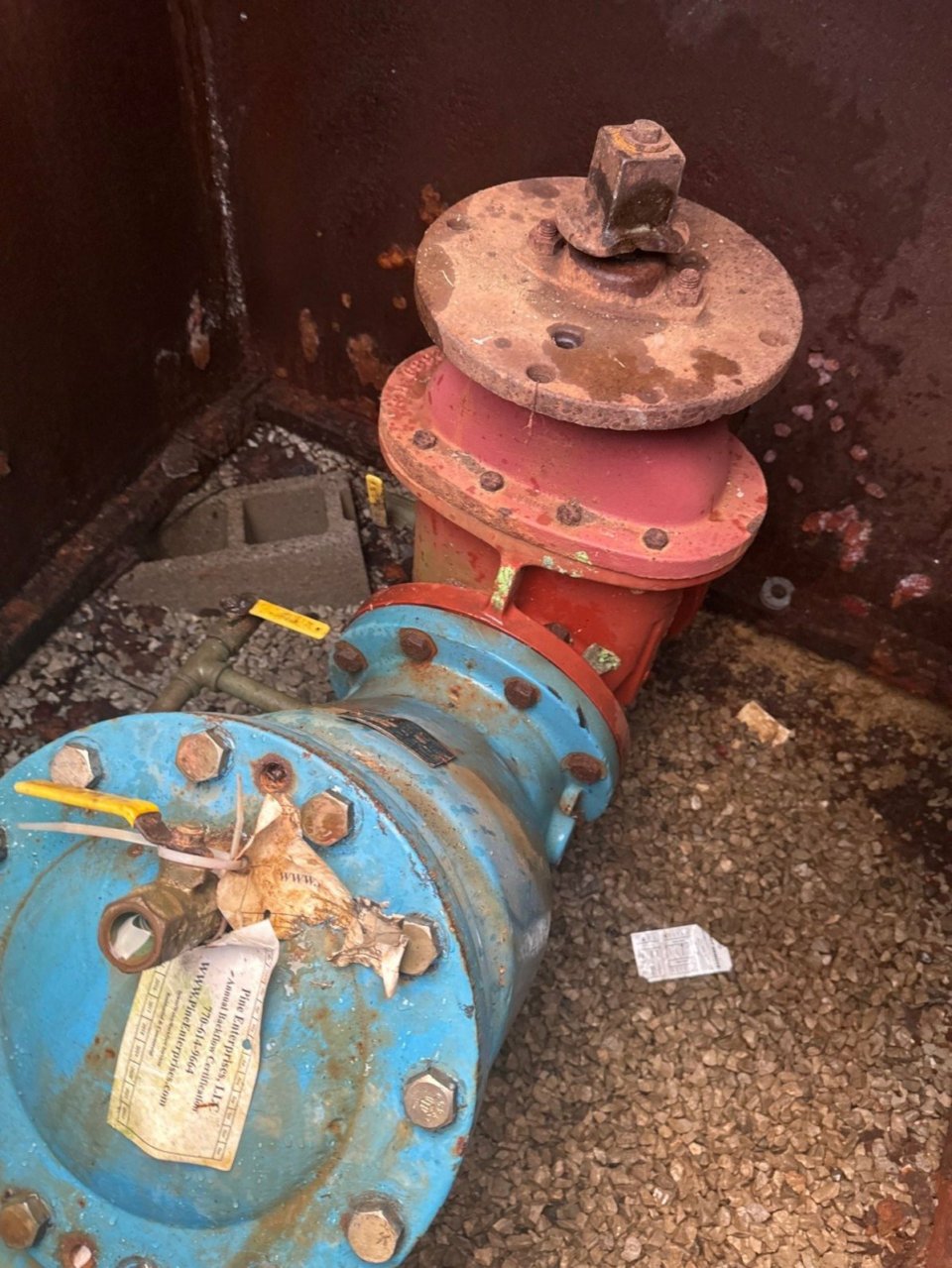 Backflows-preventer Assembly in a square vault in the ground. The falf is half plue etal and half red.