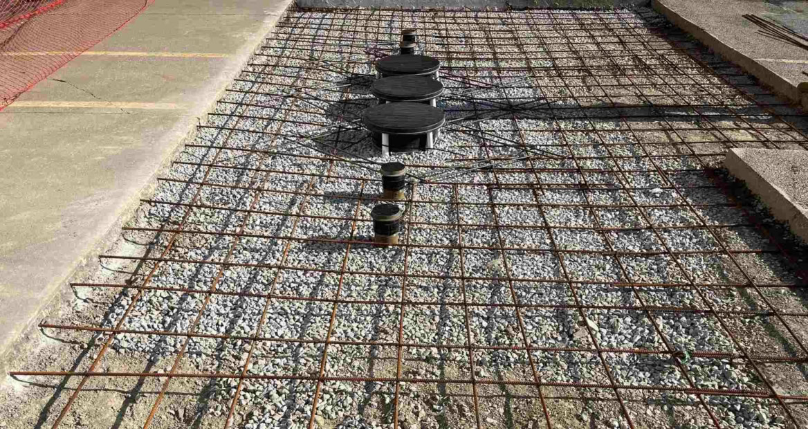 Rebar grid covering a large, rectangular section cut out of a concrete pad and backfilled with stone.