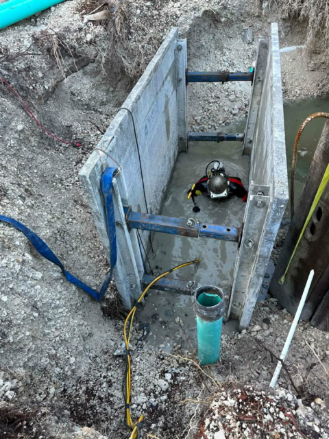 Person in diving suit within an excavation, and protected by a trench box.