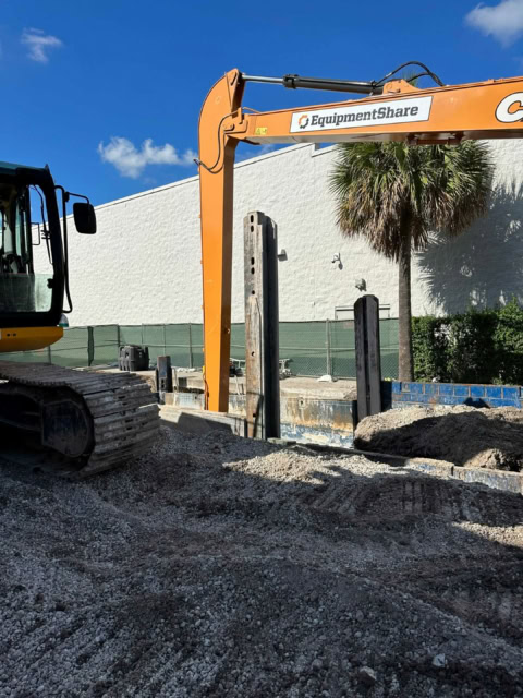 Excavator installing the side rails of a trench box to protect an excavation beside a large commercial facility.